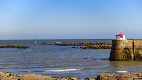 Lighthouse by sea against clear sky