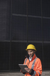 Young female engineer wearing hardhat using tablet pc in front of solar panels