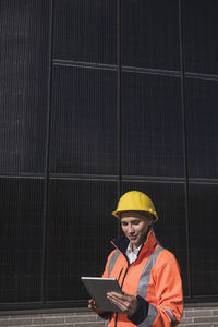 Young female engineer wearing hardhat using tablet pc in front of solar panels