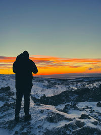 Rear view of silhouette man standing at beach against sky during sunset