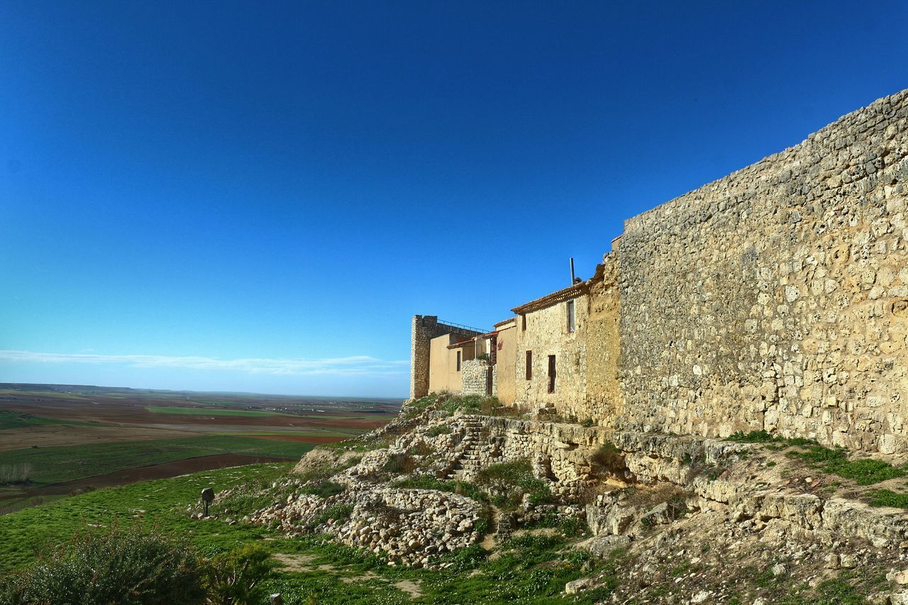 architecture, clear sky, built structure, building exterior, blue, copy space, history, old, old ruin, the past, grass, stone wall, day, sunlight, landscape, house, low angle view, sky, plant, nature