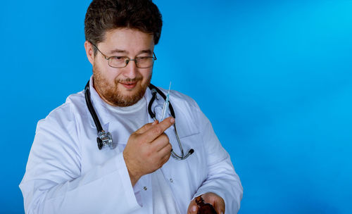Doctor holding syringe against blue background
