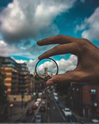 Close-up of hand holding cityscape against sky