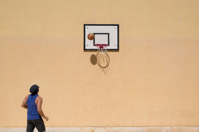 Rear view of man playing basketball against wall