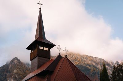 Low angle view of church building against mountain, clouds and sky