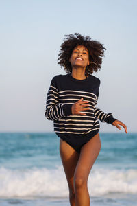 Woman with afro hair having fun at the beach running from the waves