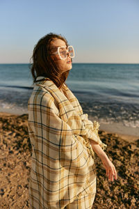 Young woman standing at beach against sky