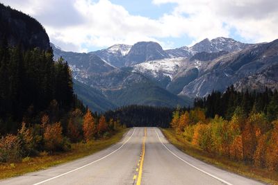 Empty road amidst trees leading towards mountains