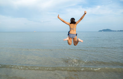 Rear view of man jumping on beach against sky