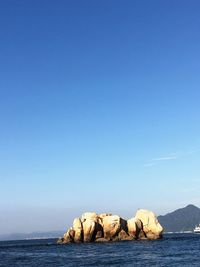 Rock formation in sea against clear blue sky