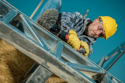 Manual worker drilling in railing against clear sky