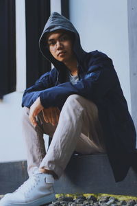 Low angle portrait of young man sitting on seat against wall