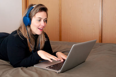 Smiling young woman using phone while sitting on laptop