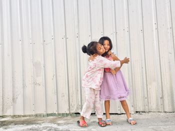 Portrait of smiling siblings embracing while standing against wall