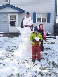 Portrait of man standing by snowman and children outside house