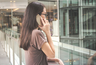 Woman talking on mobile phone while standing by railing in shopping mall