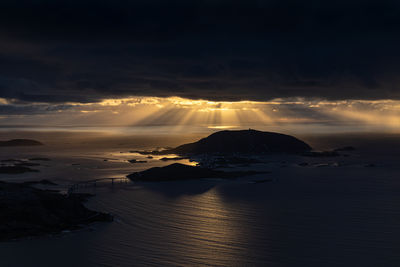 Scenic view of norwegian sea against dramatic sky during sunset with lights effects on rippled water