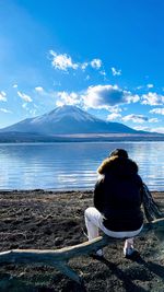 Rear view of woman sitting by sea against sky