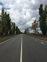 Empty road by trees against sky