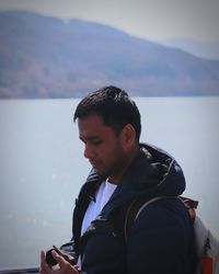 Side view of young man looking at lake against mountains