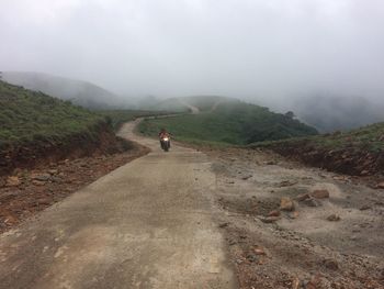 Rear view of man riding motorcycle on road against sky