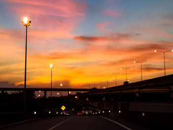 Illuminated street against sky during sunset