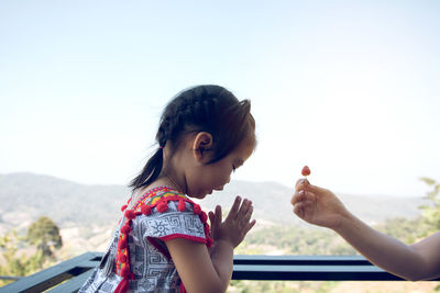 Cropped hand of mother giving food to daughter against clear sky