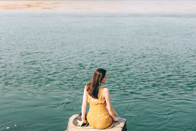 Rear view of woman sitting on rock by sea