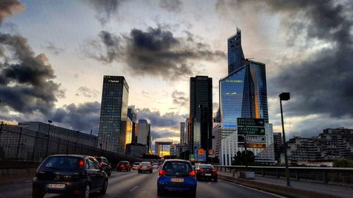 Cars on road in city against cloudy sky