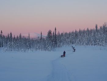 People on snow covered field against sky during sunset