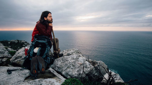 Man sitting on rock by sea against sky