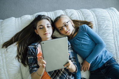 High angle view of sisters using tablet computer while lying on bed at home