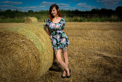 Woman leaning on hay bale against sky
