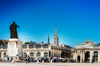 People walking on town square by statue against sky