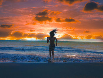 Full length of man standing on beach against sky during sunset