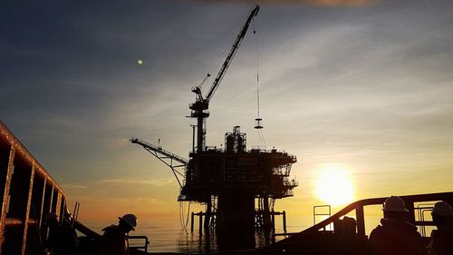 Silhouette cranes at commercial dock against sky during sunset