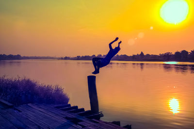 Full length of silhouette man jumping in lake against sky during sunset