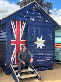 Portrait of man sitting at hut with britain flag on door