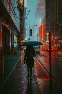 Rear view of woman walking on wet road in rainy season