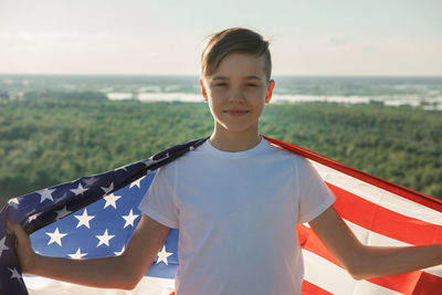 Portrait of boy holding flag against landscape