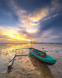 Boat moored on shore against sky during sunset