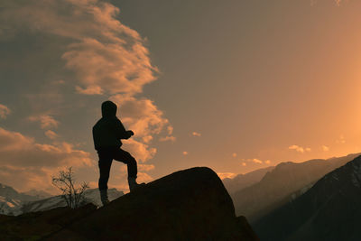 Rear view of man standing on mountain against sky during sunset