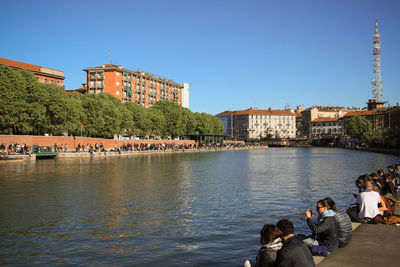 People at riverbank against clear sky