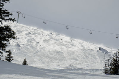 Low angle view of ski lift over snowcapped mountains against clear sky