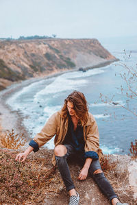 Young woman sitting on beach against clear sky