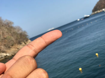 Person hand by sea against clear sky