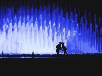 Silhouette men against illuminated blue sky at night