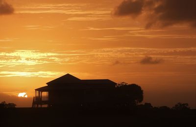 Silhouette house by tree against orange sky