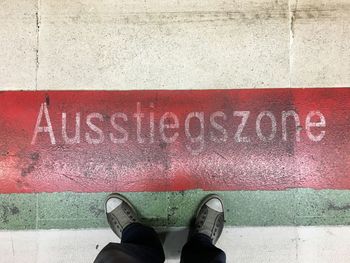 Low section of man standing by text on railroad station at frankfurt international airport
