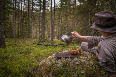 Man pouring coffee into a wooden cup while resting in a forest 